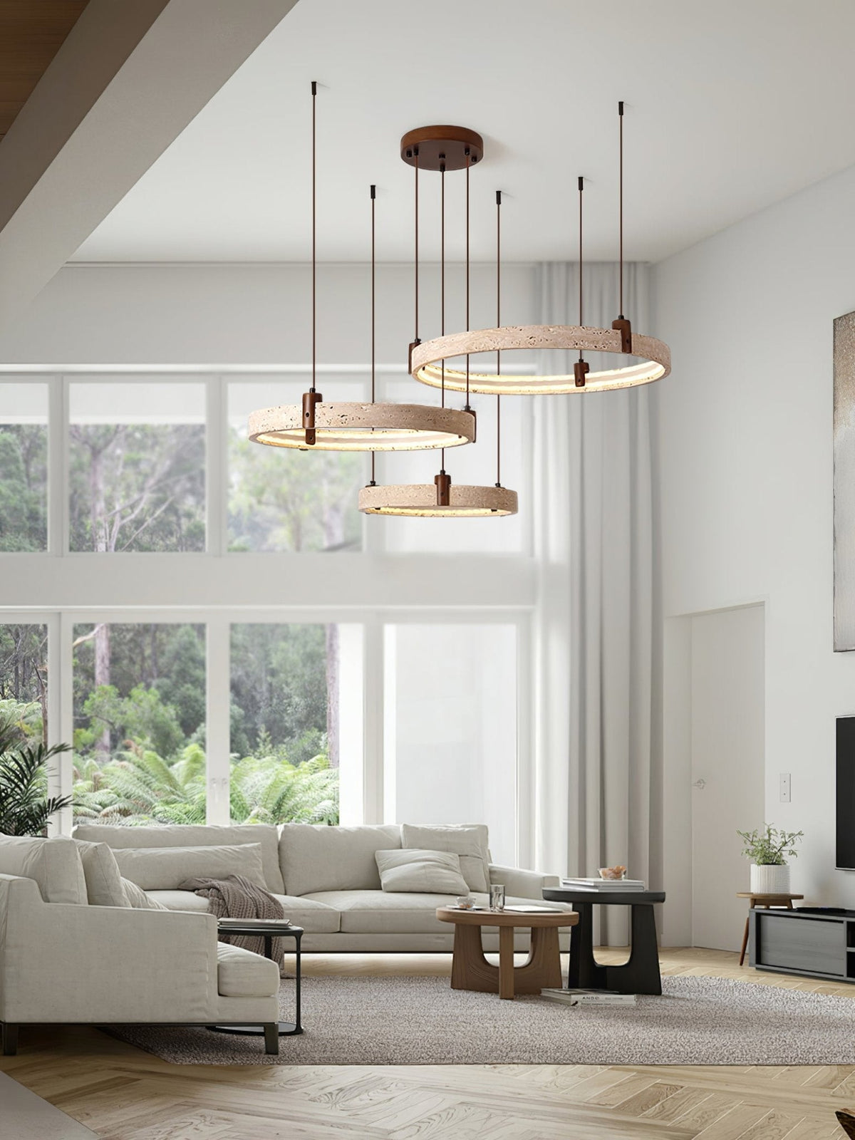 Lit travertine rings from Clérachic hang in a bright open-plan room with a high ceiling, glass walls and a large sofa below.