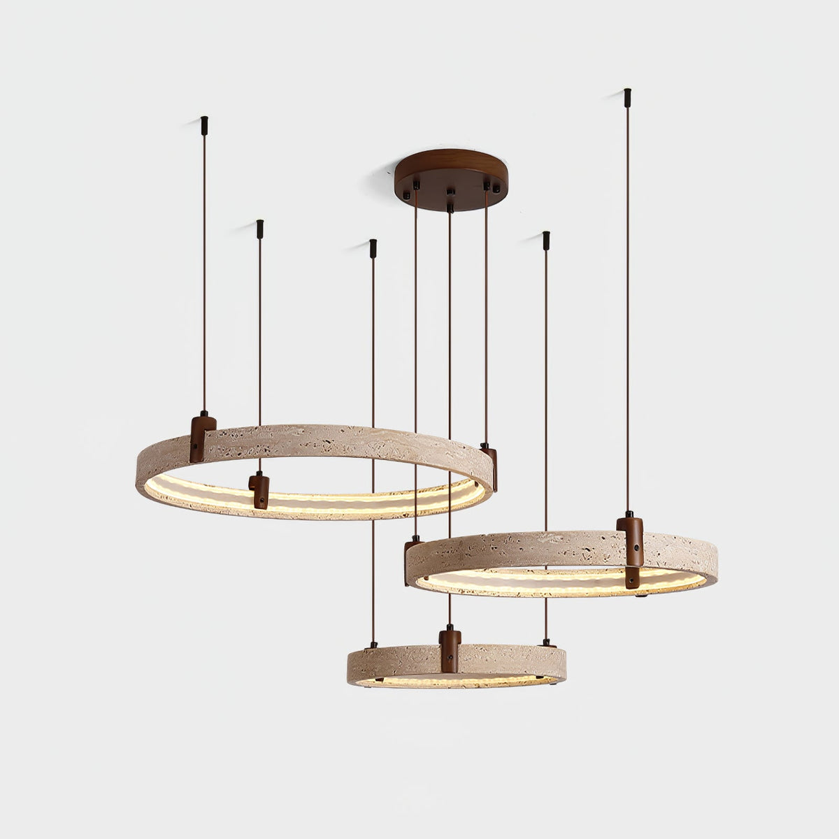 Switched on, the three travertine rings of this Clérachic pendant glow warm along their inner edge, on a pale grey backdrop.