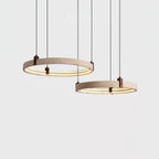 Cropped view of two stacked travertine rings on a Clérachic pendant, hung from brown cords against a light grey wall.