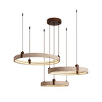 Three travertine rings on a Clérachic pendant, lit warm and hung at different heights from a round canopy, on white.