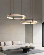 Two travertine rings from Clérachic hang above a low white sofa and black oval table, in front of a concrete wall with slim vertical slats.