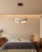 This Clérachic ring pendant hangs on three cords above a bed, with warm wall light and a neat bedside table close by.