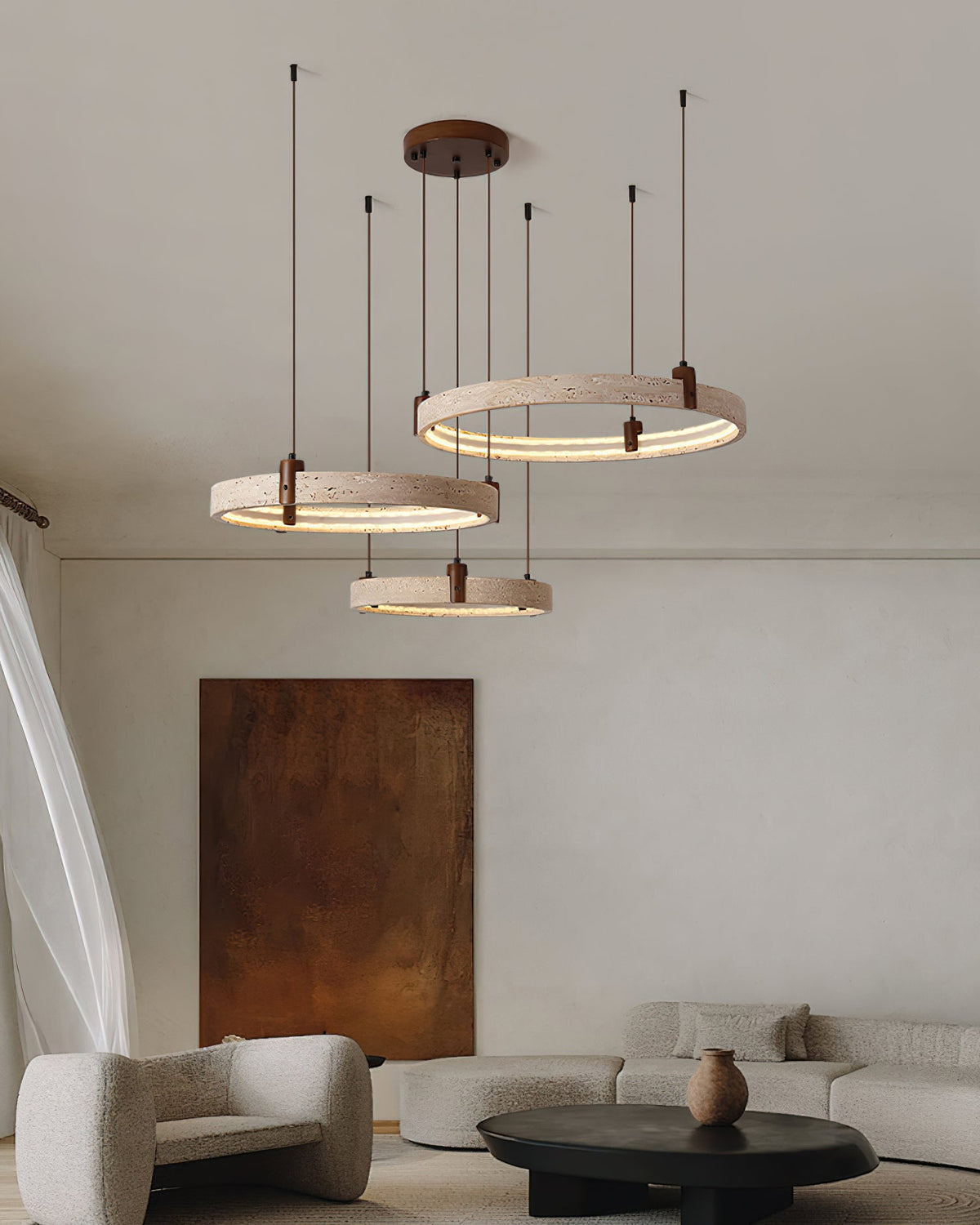 Over a living room with a rust canvas and a round black table, three travertine rings from Clérachic hang at staggered heights.