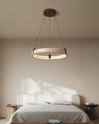 Above a bed with white linen, a Clérachic travertine ring pendant hangs from a round canopy on angled cords, in morning light.