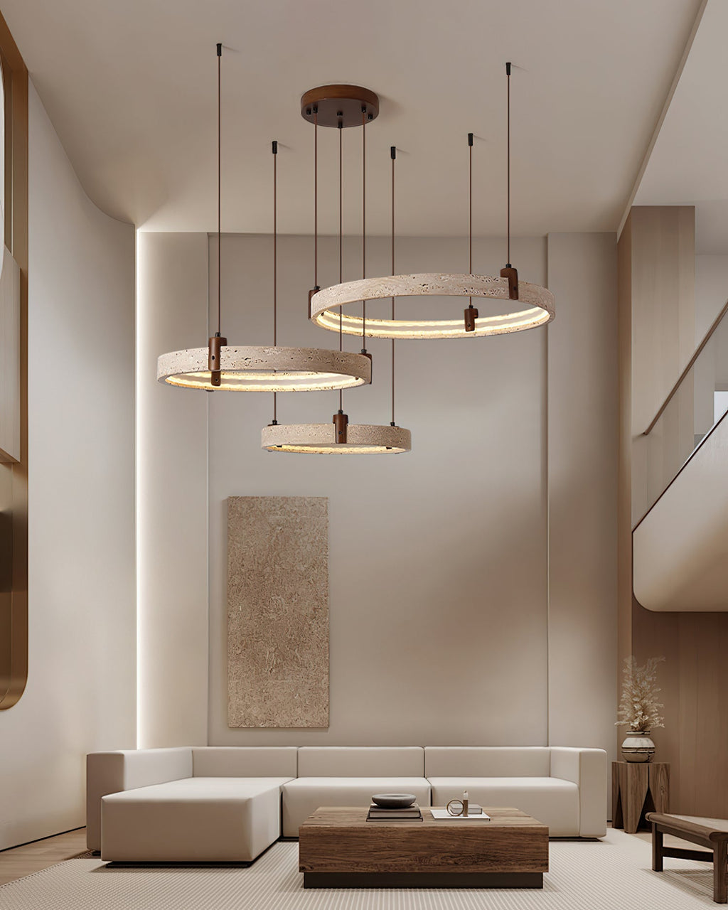 Tall interior with a beige sectional, where a Clérachic cluster of three travertine rings hangs before a stone-toned wall panel.