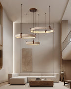 Tall interior with a beige sectional, where a Clérachic cluster of three travertine rings hangs before a stone-toned wall panel.