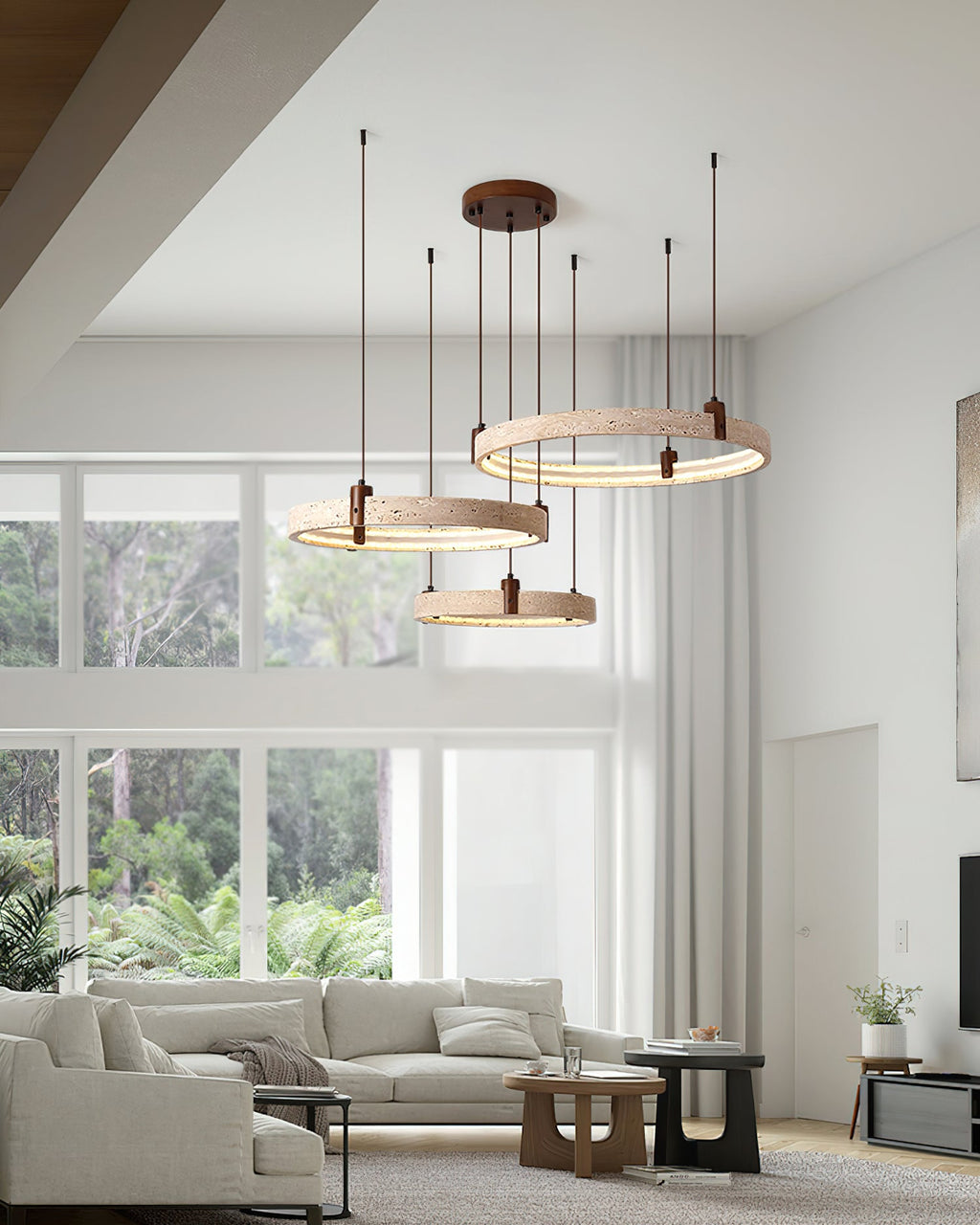 Three Clérachic travertine rings hang over a corner sofa in a bright room with big windows and a low wooden table.