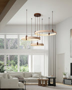 Three Clérachic travertine rings hang over a corner sofa in a bright room with big windows and a low wooden table.