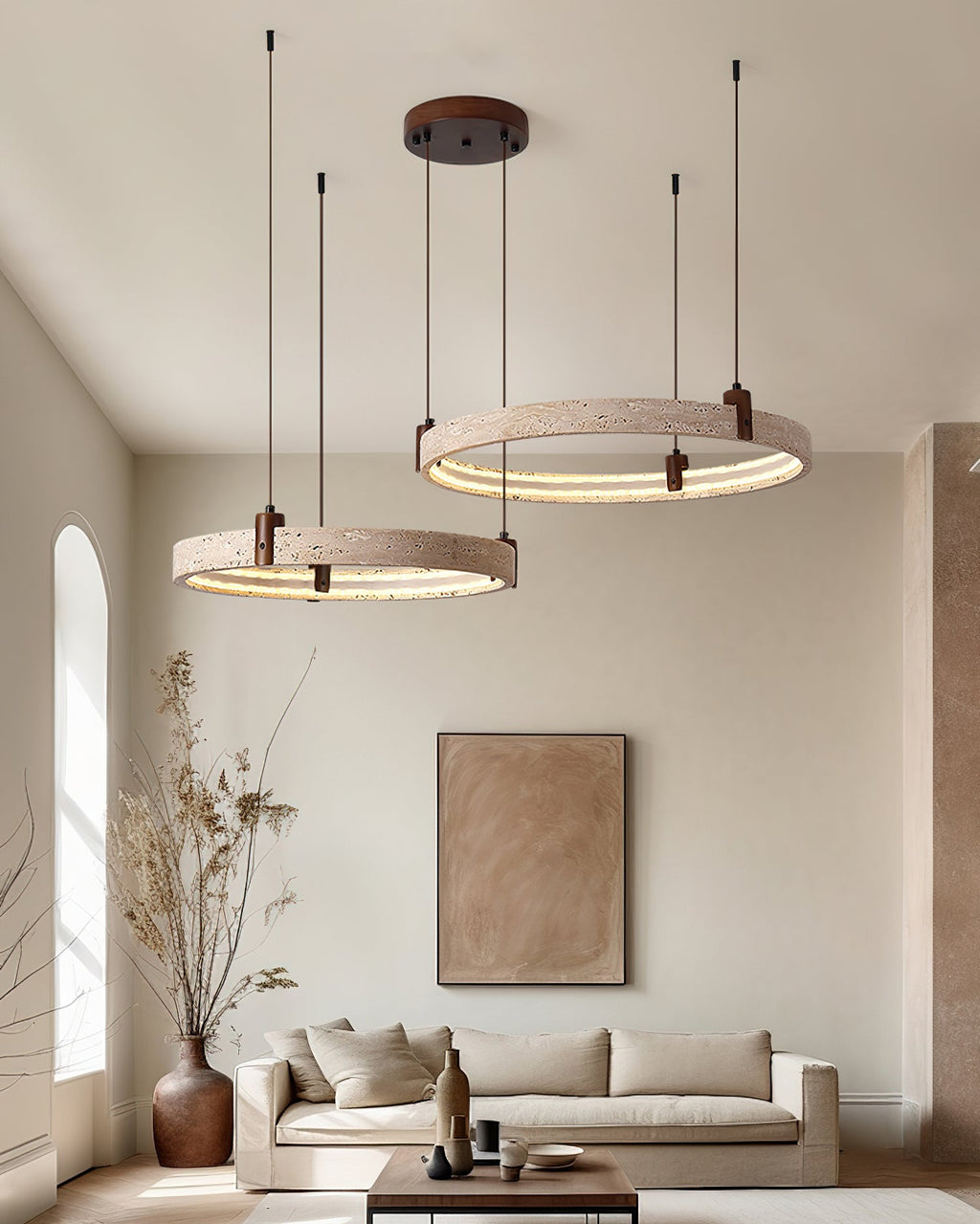 A Clérachic cluster of travertine rings hangs high in a room with a big framed print, a tall dried-stem vase and a low sofa.