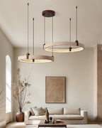 A Clérachic cluster of travertine rings hangs high in a room with a big framed print, a tall dried-stem vase and a low sofa.