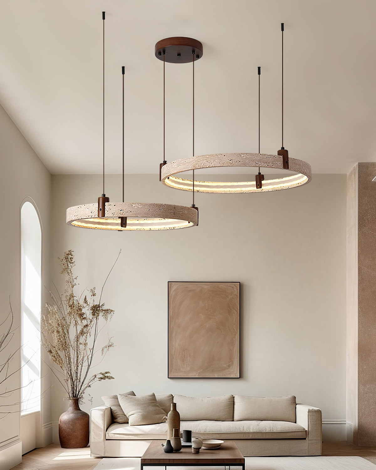 A Clérachic cluster of travertine rings hangs high in a room with a big framed print, a tall dried-stem vase and a low sofa.