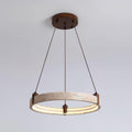 A single Clérachic travertine ring pendant hangs on three angled cords, lit warm inside, against a pale blue-grey backdrop.