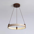A single Clérachic travertine ring pendant hangs on three angled cords, lit warm inside, against a pale blue-grey backdrop.