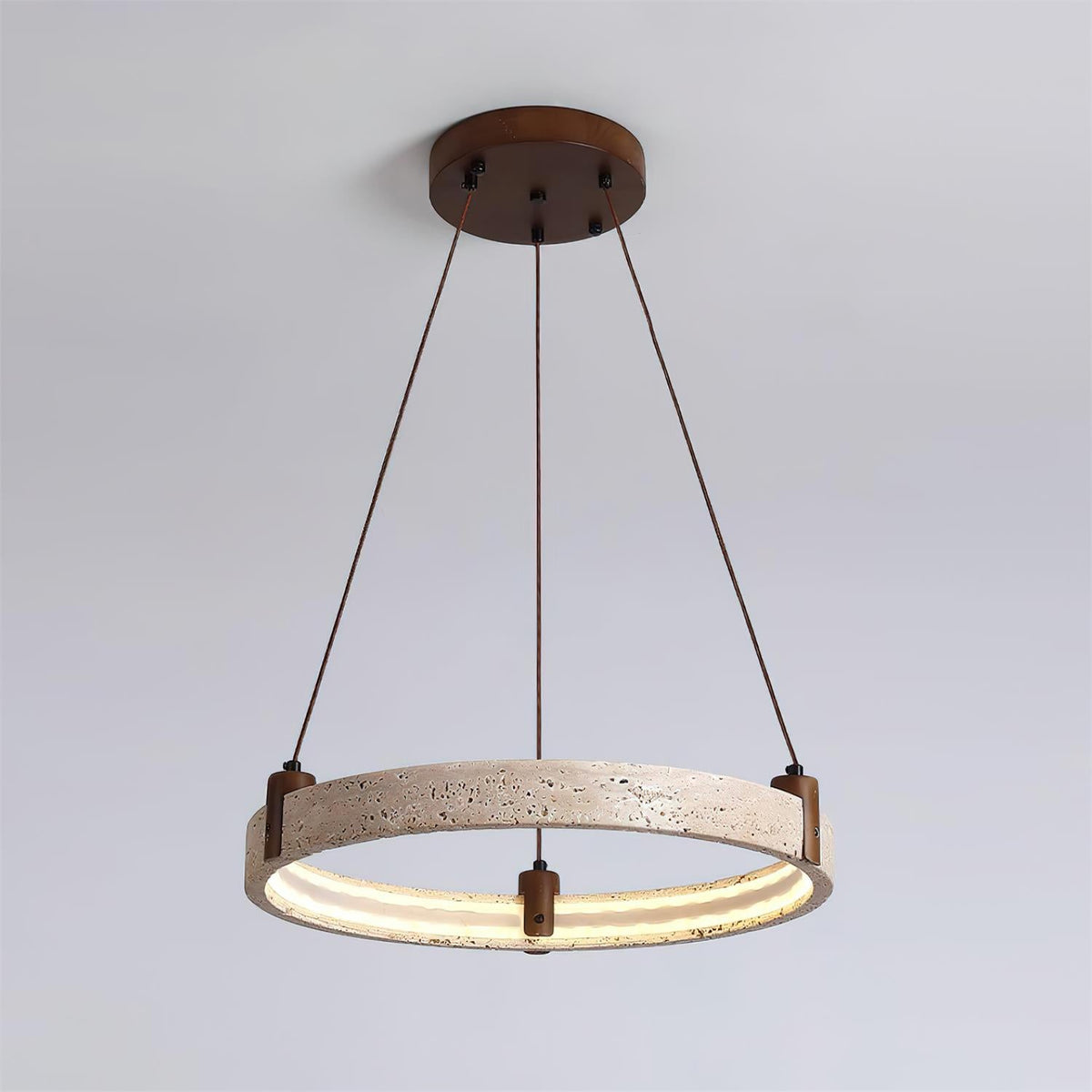 A single Clérachic travertine ring pendant hangs on three angled cords, lit warm inside, against a pale blue-grey backdrop.