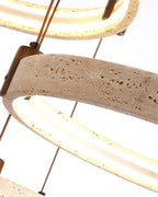 Tight view of a lit travertine ring on a Clérachic pendant, with a pitted stone face, a walnut bracket and a warm light band.