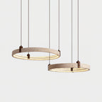 Two lit travertine rings from Clérachic hang on straight cords, one above the other, in front of a pale grey backdrop.