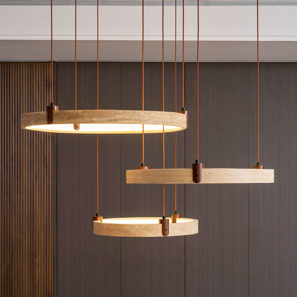 Three golden-toned travertine rings from Clérachic glow in front of dark vertical wood slats, with warm light inside each ring.