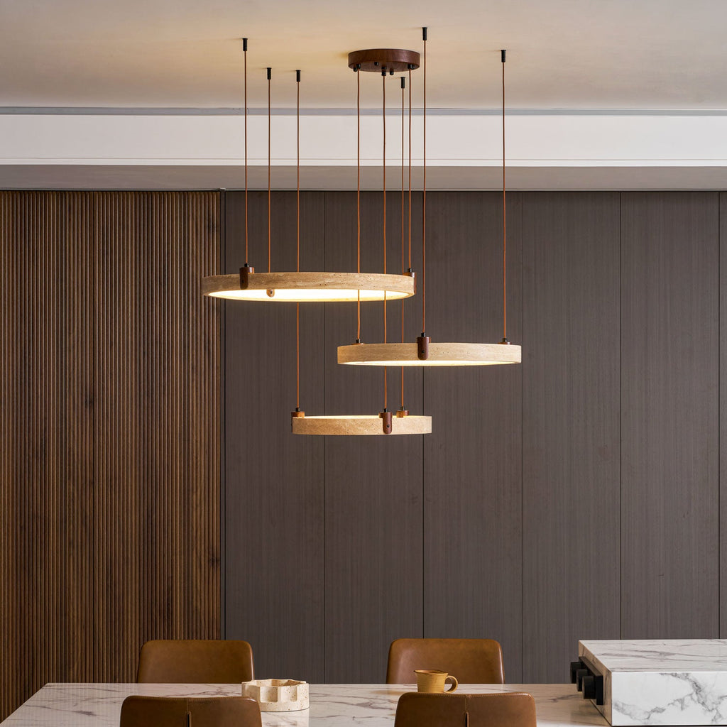 Seen at eye level, a Clérachic pendant of three travertine rings hangs over a marble-topped table and tan leather chairs.
