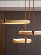 Three golden travertine rings of this Clérachic pendant hang close to the camera against dark wood panelling, lit warm.