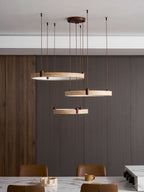 Further back, the three travertine rings of this Clérachic pendant hang over a marble dining table with brown leather chairs.