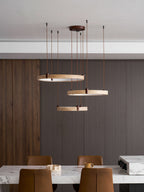 Wide view of three travertine rings from Clérachic over a marble table and leather chairs, with dark slats behind.
