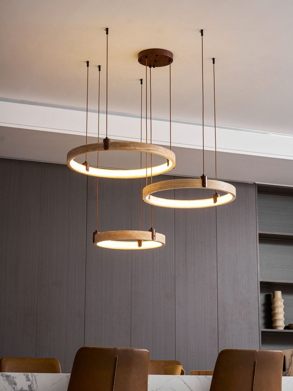 This Clérachic travertine pendant glows warm across all three rings, hung over a dining table with a marble top and leather chairs.