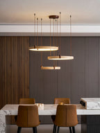 Three golden travertine rings on a Clérachic pendant hang in a modern dining room, with their cords reaching up to a pale ceiling.
