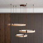 From the side, the three golden travertine rings of this Clérachic pendant hang in front of a dark wood wall.