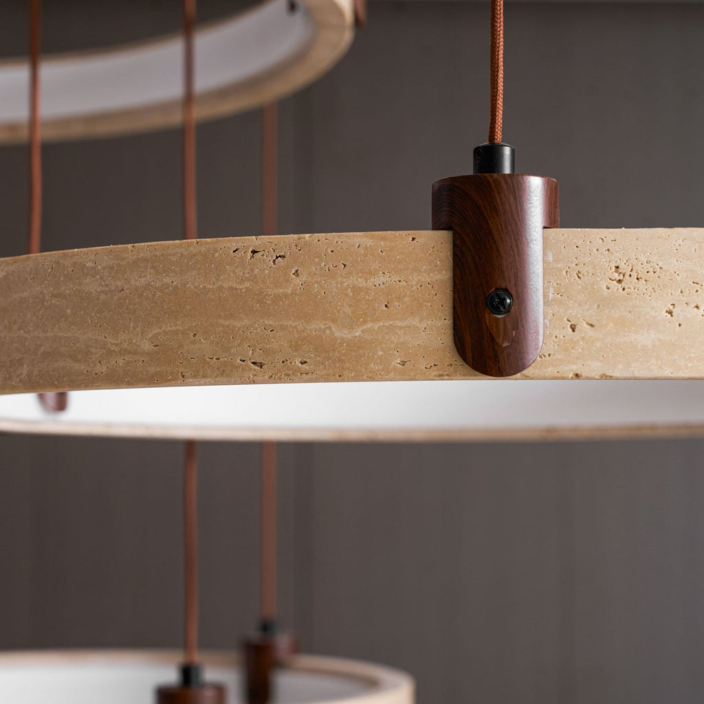 Lit from within, two of the travertine rings on this Clérachic pendant hang close to the camera, with a dark wood wall behind.