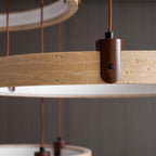 Lit from within, two of the travertine rings on this Clérachic pendant hang close to the camera, with a dark wood wall behind.