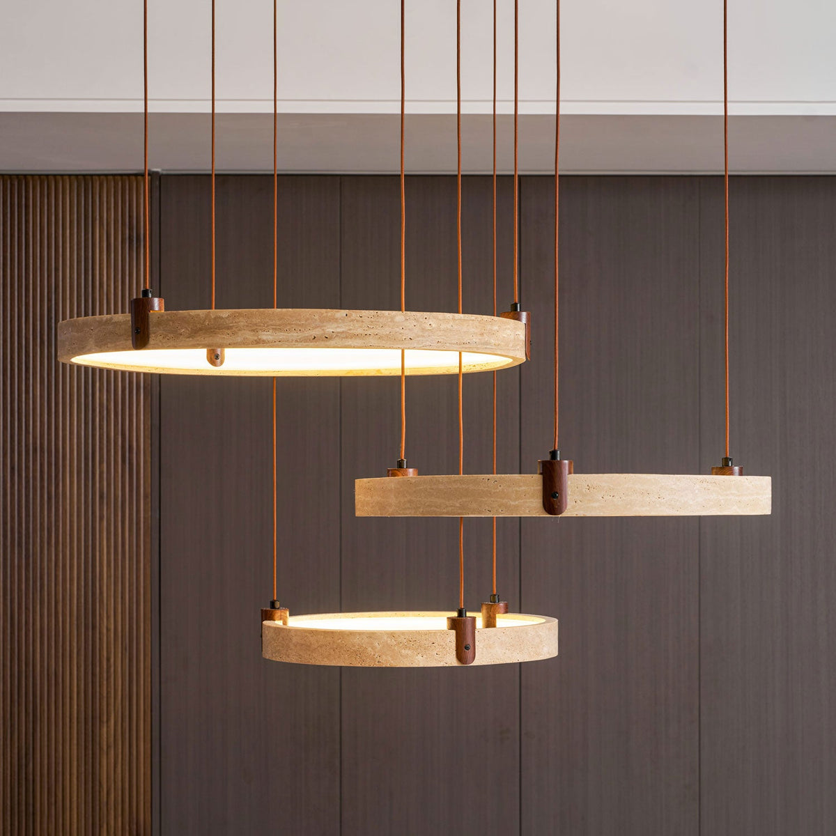 Close view of a golden travertine ring with natural pits and a walnut bracket on this Clérachic pendant, with brown cords above it.