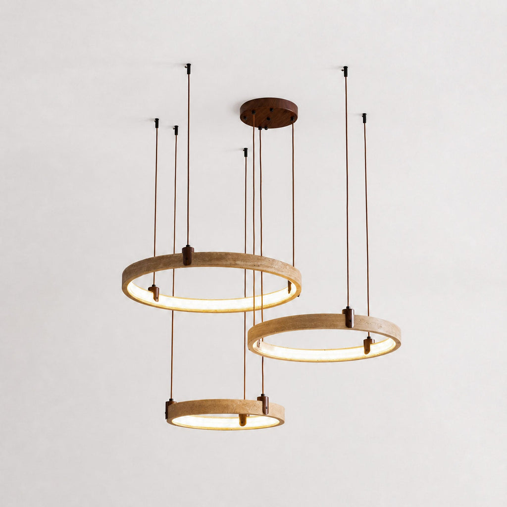 Three golden-toned travertine rings from Clérachic hang on brown cords from a round canopy, lit warm, against a pale plaster wall.