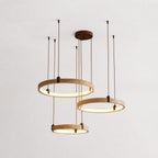 Three golden-toned travertine rings from Clérachic hang on brown cords from a round canopy, lit warm, against a pale plaster wall.