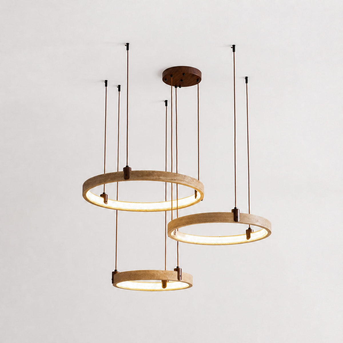 Three golden-toned travertine rings from Clérachic hang on brown cords from a round canopy, lit warm, against a pale plaster wall.
