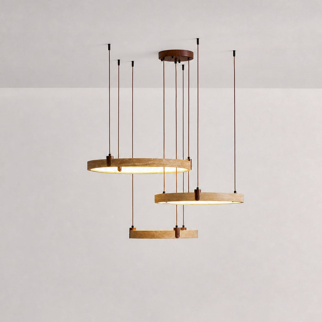 Studio shot of three golden travertine rings on a Clérachic pendant, with the lower ring lit warm, on a soft pink-grey backdrop.