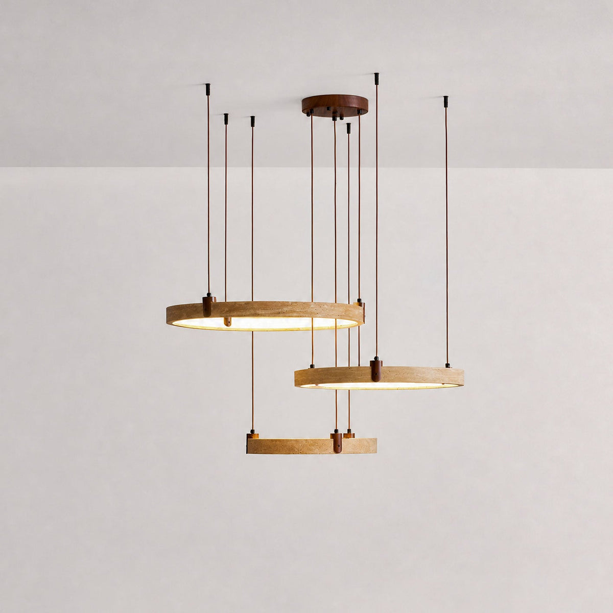 Studio shot of three golden travertine rings on a Clérachic pendant, with the lower ring lit warm, on a soft pink-grey backdrop.