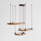 A Clérachic pendant of three golden travertine rings hangs from a small round canopy, seen from slightly below on a pale backdrop.