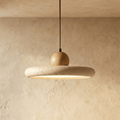 Clérachic travertine disc pendant, speckled stone ring with a round wood knob on top, lit from below against limewash.