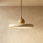 Clérachic travertine disc pendant, speckled stone ring with a round wood knob on top, lit from below against limewash.