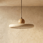 Clérachic pendant with a speckled travertine disc and a round oak-toned wood ball, switched off against a plaster wall.