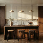 Three Clérachic travertine disc pendants in a row above a walnut kitchen island, with stools and a marble splashback.