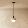 Clérachic pendant light with a pitted stone dome shade and dark walnut ball finial, glowing softly.