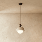 Clérachic pendant light with a pitted stone dome shade and dark walnut ball finial, glowing softly.