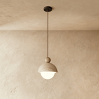 A front view of the Clérachic pendant light's stone dome shade and dark walnut ball against a plaster wall.