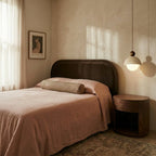 A Clérachic pendant light glows beside a bed with dusty pink linens and a walnut nightstand.