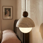 Close-up of the Clérachic pendant light's stone dome and walnut ball finial beside a bedroom headboard.