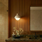 A Clérachic pendant light with a walnut cap hangs above a dark green marble vanity in a wood-panelled bathroom.