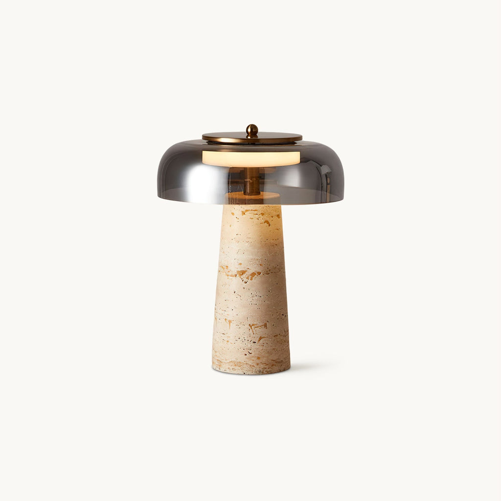 This Clérachic table lamp on a plain white backdrop, a smoky grey glass dome above a tapered beige travertine base.