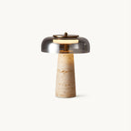 This Clérachic table lamp on a plain white backdrop, a smoky grey glass dome above a tapered beige travertine base.