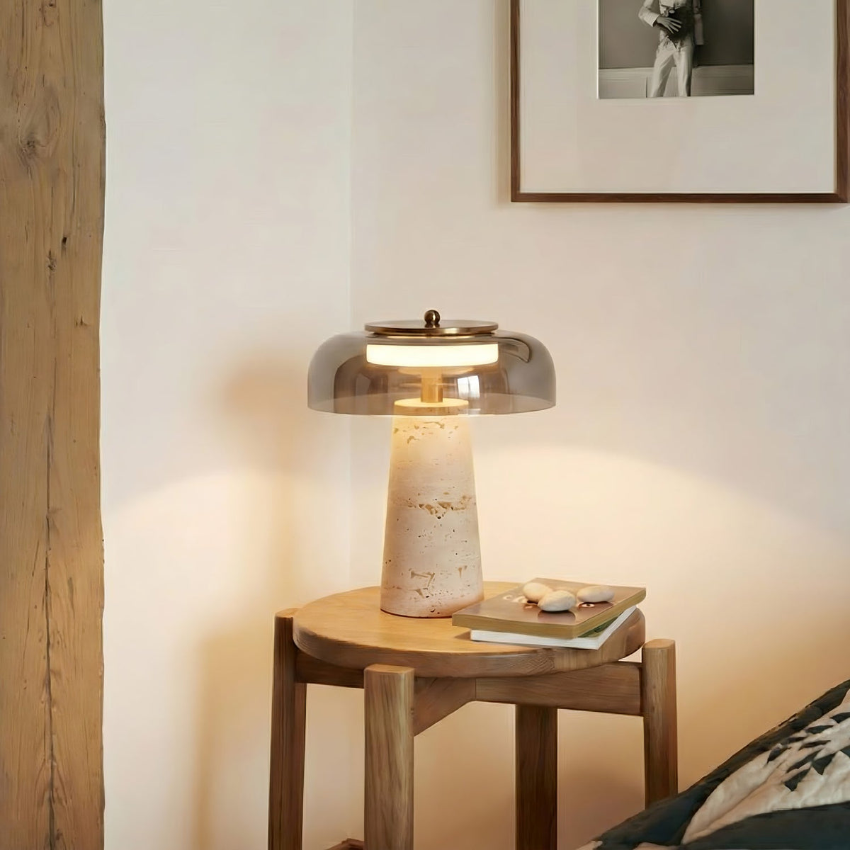 Lit Clérachic table lamp with a smoky grey dome on a wooden stool beside a framed print, with a few pebbles and a book nearby.